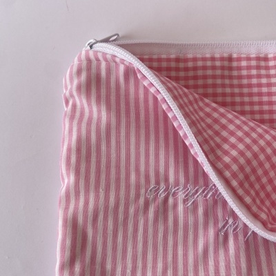 Estojo rosa com riscas verticais e interior xadrez, fecho branco e bordado branco