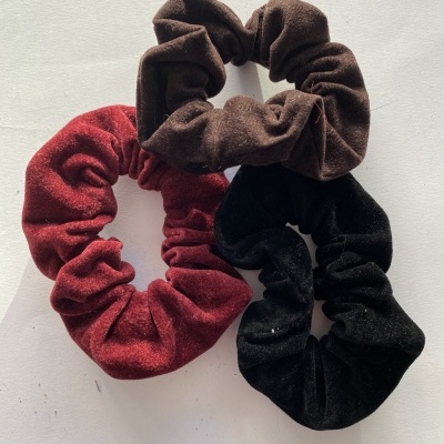 Três scrunchies de tecido aveludado nas cores castanho, vermelho escuro e preto