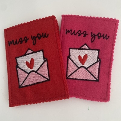 Dois retângulos de tecido vermelho e rosa com bordado de envelope e texto miss you