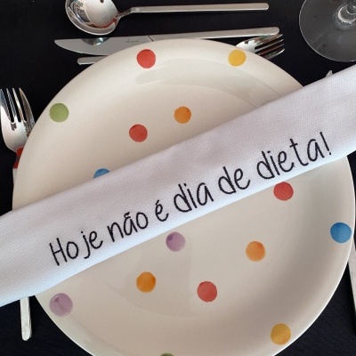 Prato com bolinhas coloridas e guardanapo branco com frase bordada sobre ele.