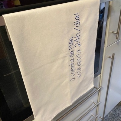 Pano de cozinha branco com texto azul pendurado na porta de forno numa cozinha branca.