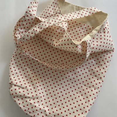 Mala tote de tecido cru com pequenos corações vermelhos.