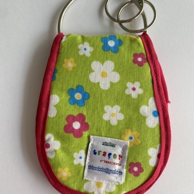 Porta-chaves de tecido verde com flores coloridas e borda vermelha com etiqueta visível