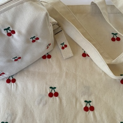 Saco de tecido com padrão de cerejas vermelhas e bolsa bege com padrão de cerejas bordadas