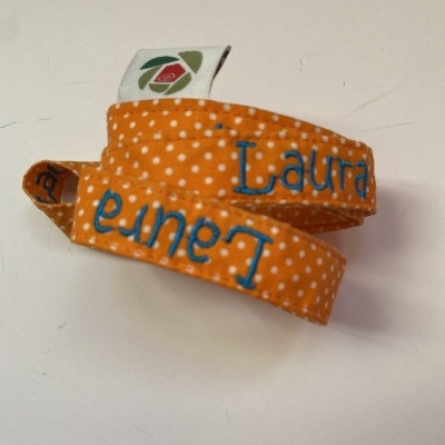 Fita de tecido laranja com bolinhas brancas e nome Laura bordado a azul