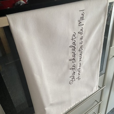 Pano de cozinha branco com bordado preto pendurado em forno