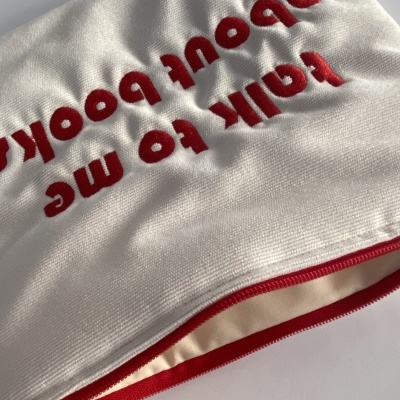 Capa branca com texto bordado vermelho e fecho de correr vermelho