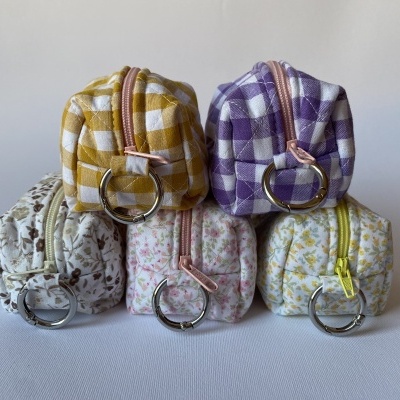 Cinco bolsos de tecido coloridos com padrão floral e xadrez e argolas metálicas.