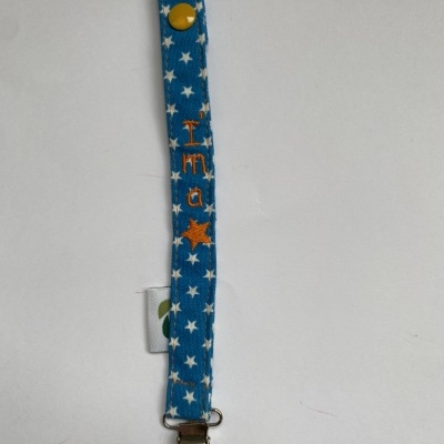 Fita azul com estrelas brancas, texto laranja 'Ina' e estrela, botão amarelo e presilha metálica