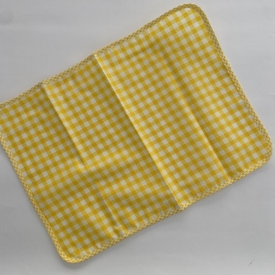 Manta rectangular amarela com padrão de quadrados brancos.