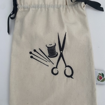 Saco de tecido cru com desenho de agulhas, tesoura e linha.