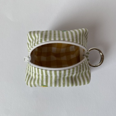Bolsa pequena riscada verde e branca com fecho aberto e argola metálica.