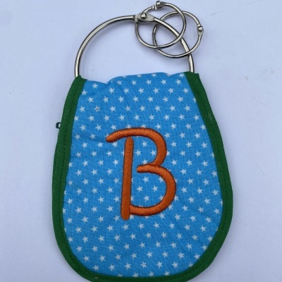Estojo azul com estrelas brancas, bordas verdes, letra B laranja e argolas metálicas