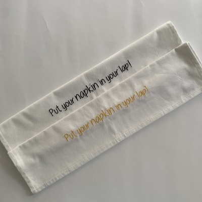 Guardanapos de tecido branco com frases bordadas em preto e amarelo