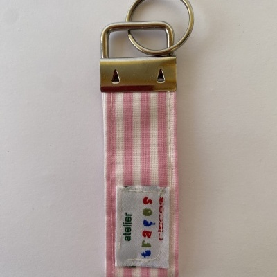 Porta-chaves em tecido rosa às riscas brancas com etiqueta colorida e suporte metálico prateado.