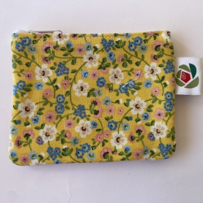 Carteira de tecido amarelo com padrão floral colorido e etiqueta lateral com desenho de flor