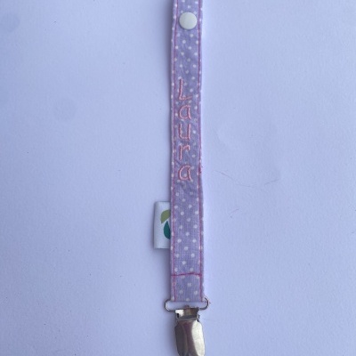 Alça de tecido lilás com fecho metálico e nome Laura bordado.