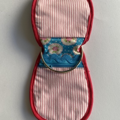 Estojo pequeno de tecido com riscas rosa e branco, bordas vermelhas e anel metálico