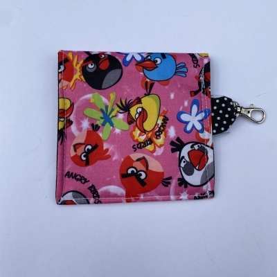 Carteira rosa com personagens Angry Birds e pingente preto com bolinhas brancas.