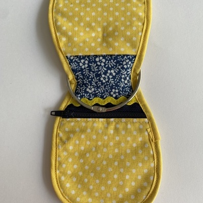 Estojo amarelo com bolinhas brancas aberto, mostrando interior azul com flores brancas, fecho metálico e zíper preto