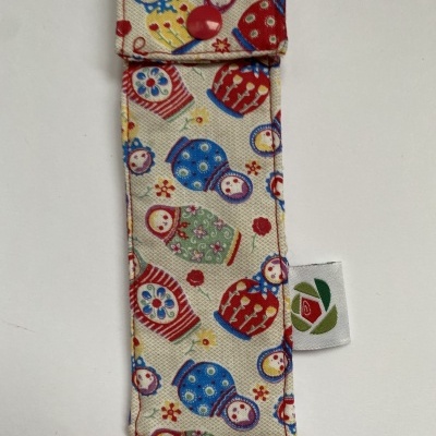 Estojo de tecido bege com padrão de bonecas russas coloridas e botão vermelho