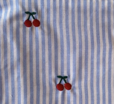 Tecido azul e branco com bordados de cerejas vermelhas.