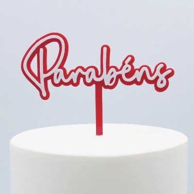 Topo de bolo vermelho com a palavra Parabéns numa caligrafia cursiva sobre bolo branco