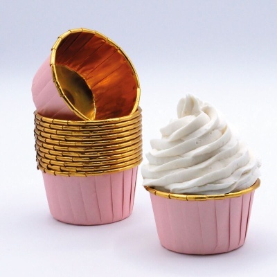 Forminhas para cupcakes rosa com interior dourado e uma com creme branco em espiral.