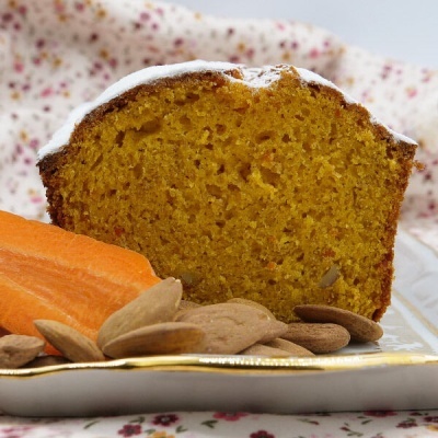 Fatia de bolo de cenoura com açúcar em pó, cenoura e amêndoas numa travessa sobre tecido floral