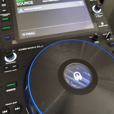 Leitor DJ Denon DJ com superfície preta, luzes azuis e ecrã digital com texto