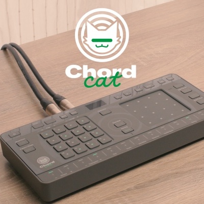 Controlador MIDI preto com botões e pads sobre mesa de madeira com logotipo 'Chord cat'