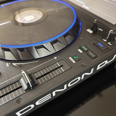 Controlador de DJ preto com luz azul no prato giratório e diversos botões e controles