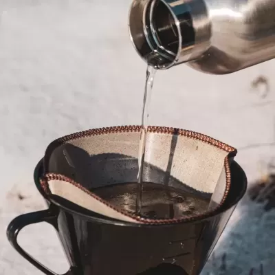 Filtro de café de pano em chávena preta com água a ser vertida de garrafa de aço inoxidável