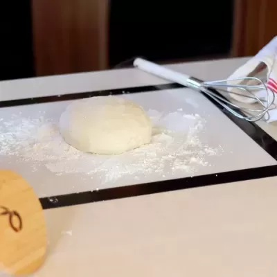 Bola de massa branca com farinha e batedor de metal numa superfície clara