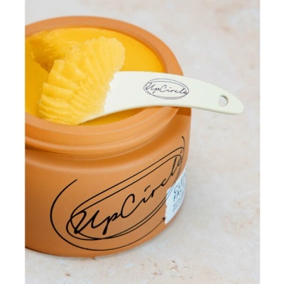 Pote de barro castanho com creme amarelo e espátula branca marca UpCircle