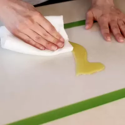 Mãos a limpar líquido amarelo de superfície branca com pano