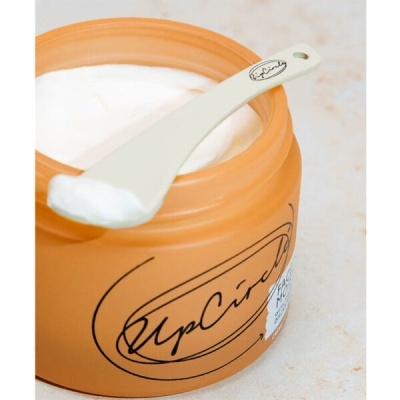Frasco laranja fosco de creme facial com colher branca e creme branco