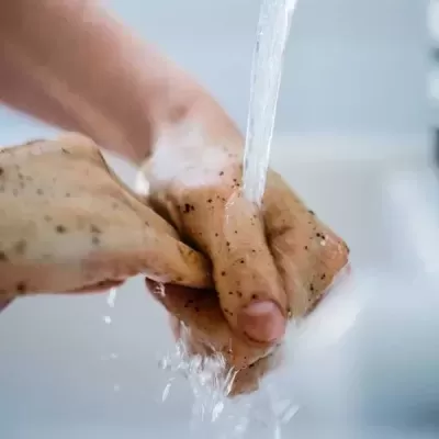 Mãos a serem lavadas com água corrente e partículas escuras na pele