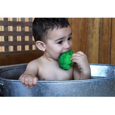 Criança nua num tanque metálico a morder um brócolis verde