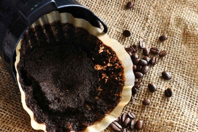 Filtro de papel com borra de café usado e grãos de café sobre tecido de juta.