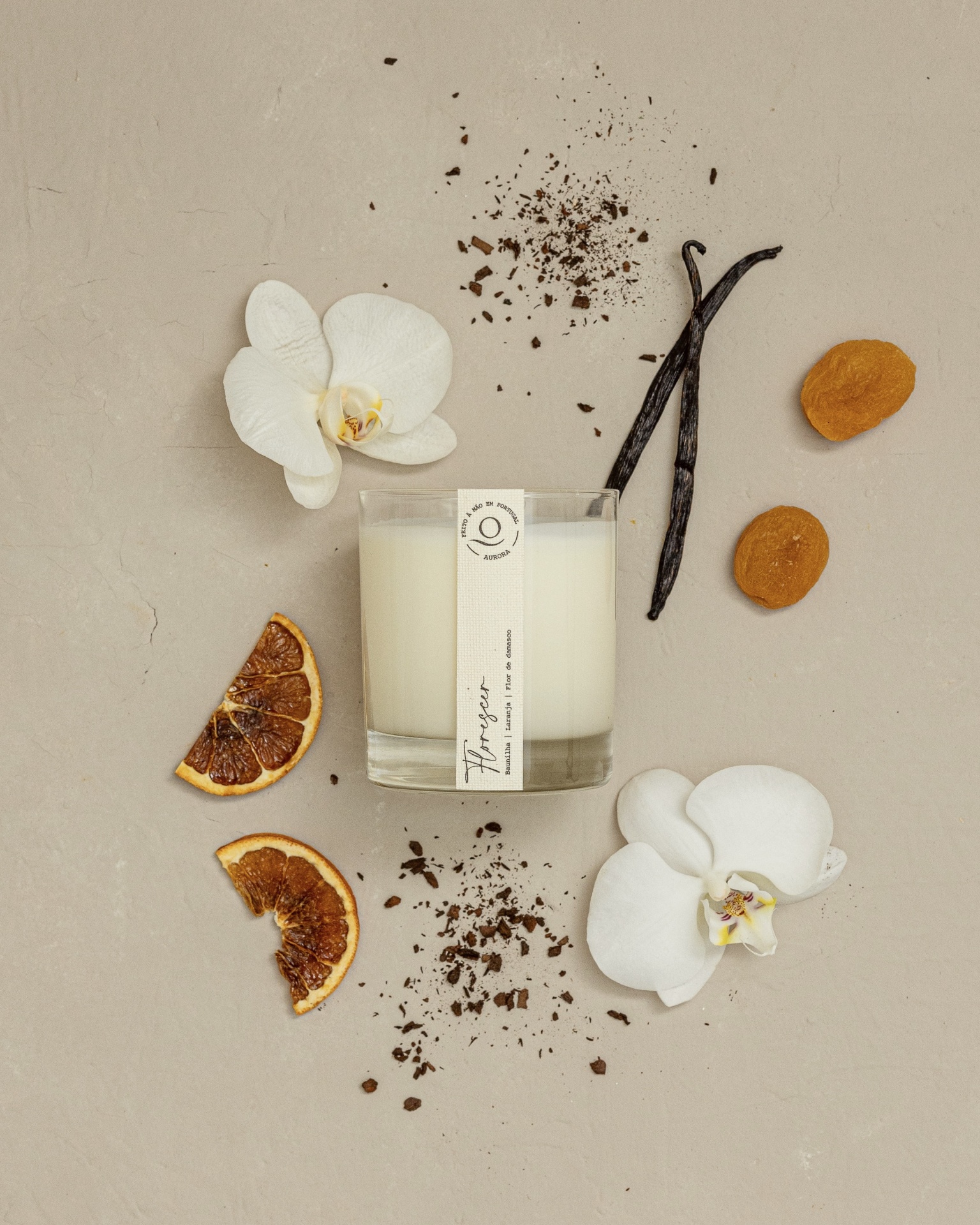 Vela Aromática Vela perfumada branca em copo de vidro com flores de orquídea, baunilha, laranja seca e pedaços castanhos ao redor