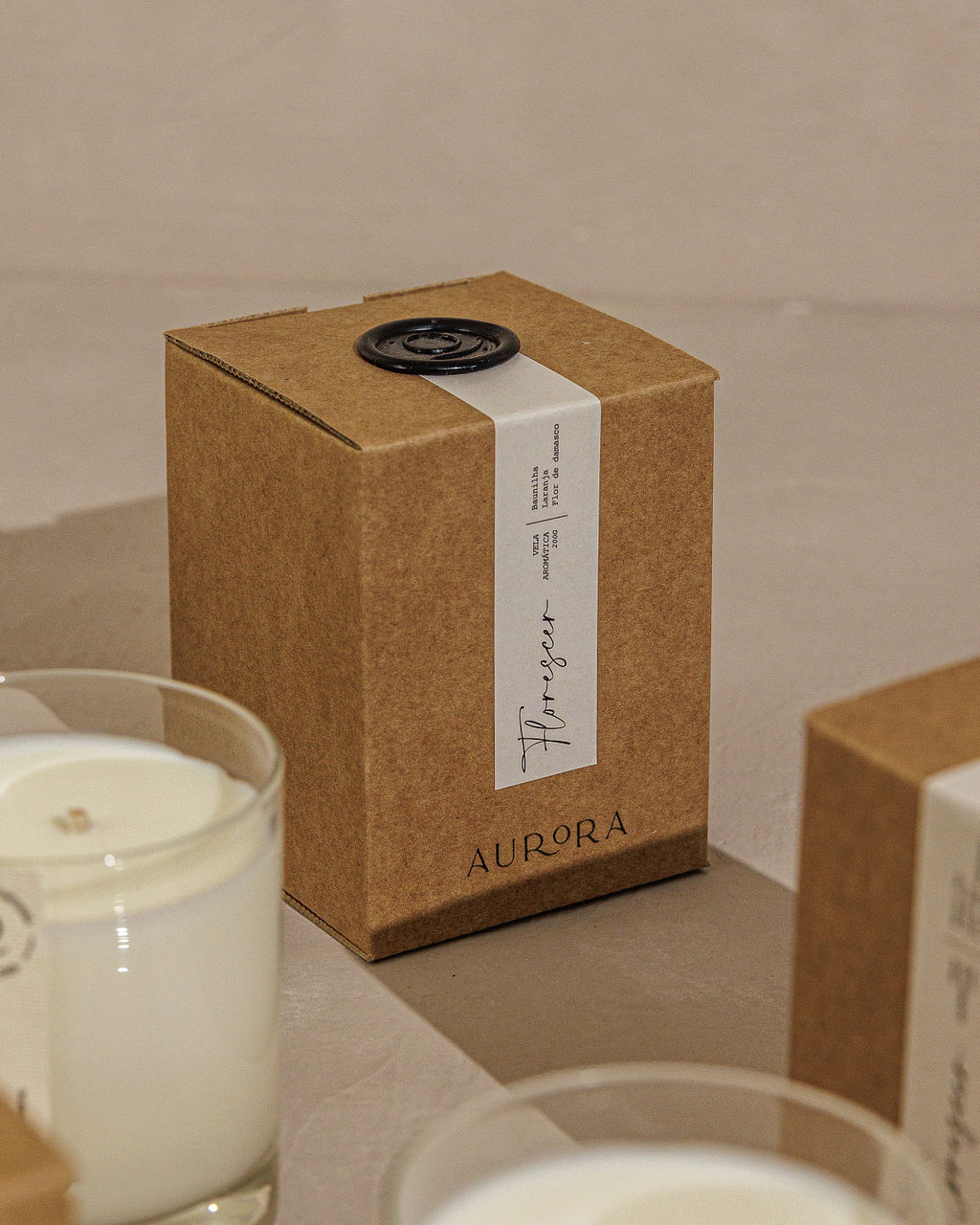 Vela Aromática Caixa castanha com etiqueta branca e velas brancas em copos.