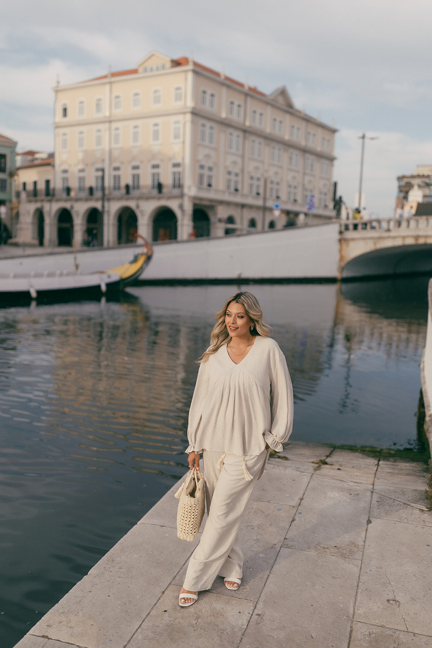 Blusa Serena Mulher com roupa branca junto a canal com barco e edifício antigo ao fundo