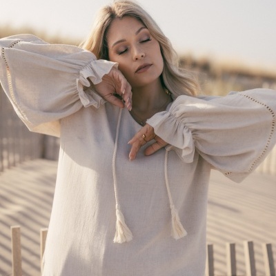 Camisa bege clara de tecido leve com mangas largas e cordões com franjas