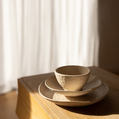 Conjunto de louça cerâmica bege com duas tigelas e um prato sobre mesa de madeira clara