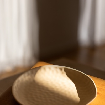 Prato cerâmico creme com textura irregular numa mesa de madeira clara