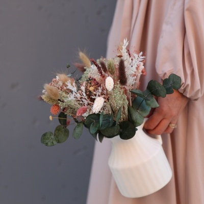 Vaso branco com flores secas coloridas seguras por pessoa com vestido rosa claro