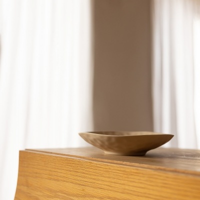 Tigela castanha de cerâmica sobre mesa de madeira clara com cortinas ao fundo