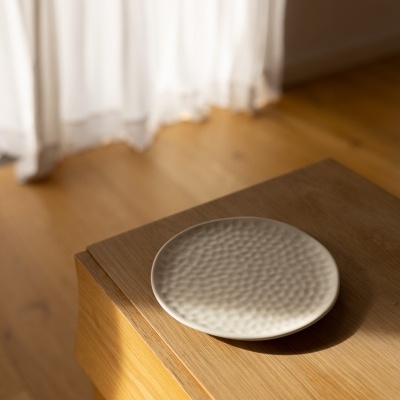 Prato cerâmico branco com textura ondulada numa mesa de madeira com cortina ao fundo