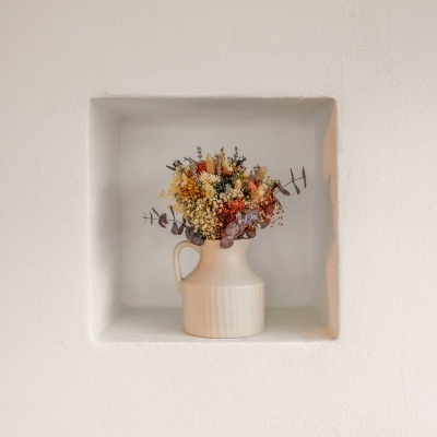 Jarro de cerâmica creme com flores secas num nicho branco na parede